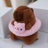 A brown capybara plush doll wearing a pink hoodie with small wings, sitting in a white box.