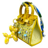 A yellow mini house-shaped bag with a puppy keychain charm and multicolored striped strap.
