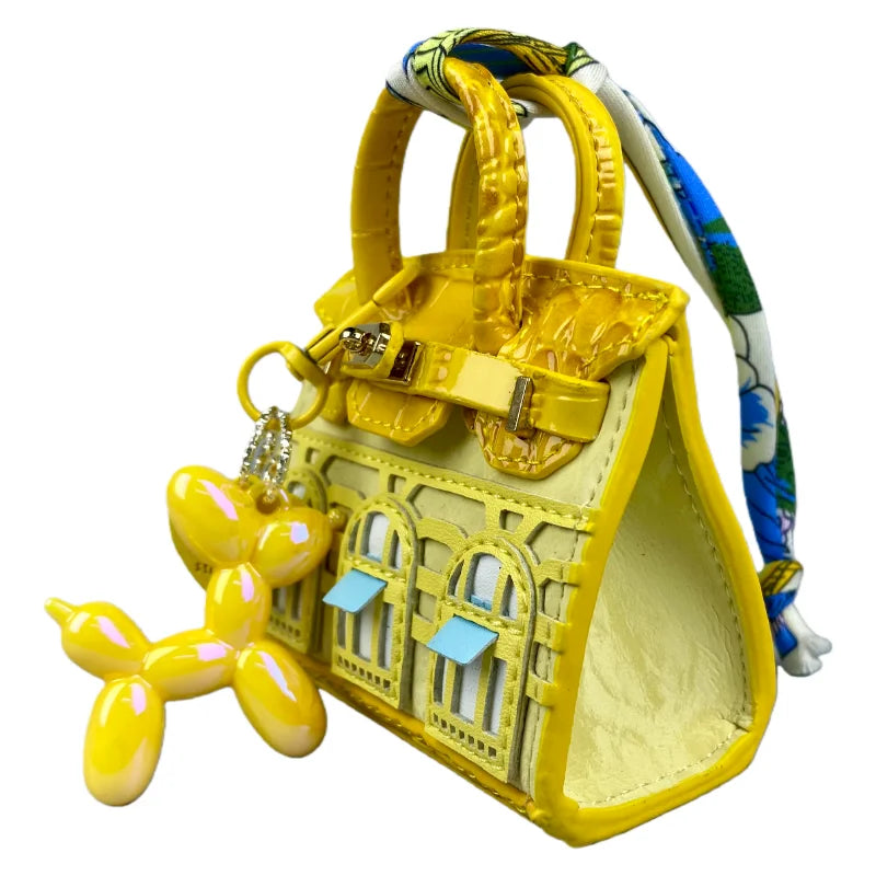 A yellow mini house-shaped bag with a puppy keychain charm and multicolored striped strap.