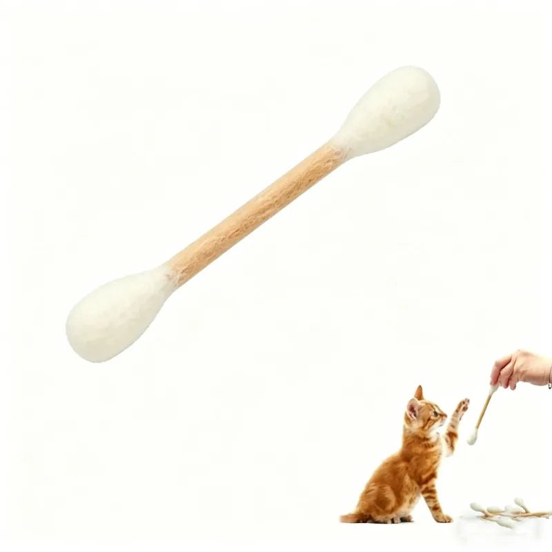 A wooden cotton swab shaped catnip toy is being used by a hand to interact with a small orange kitten.