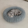 A gray tabby cat is resting inside a round, ribbed, plush pet bed.