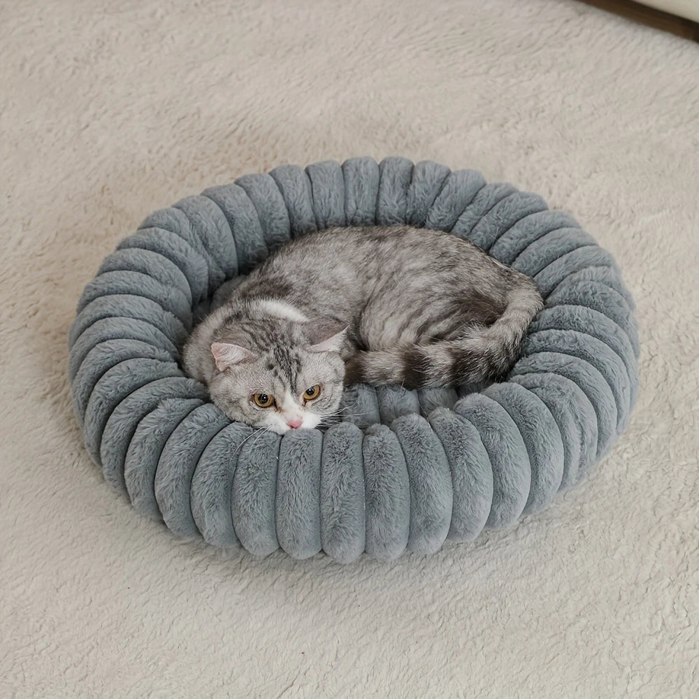 A gray tabby cat is resting inside a round, ribbed, plush pet bed.