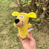 A yellow plush dog toy with large ears and a black nose is held in a person's hand outdoors.