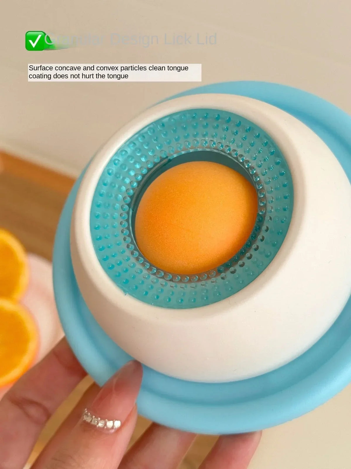 Eine Hand hält ein blaues Tier-Lickspielzeug mit orangem Zentrum, zum Reinigen der Zunge.