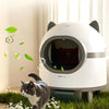 A white automatic deodorizer device is shown with a cat interacting with the surrounding greenery.