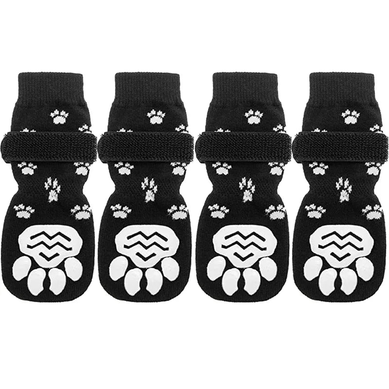 A set of four black anti-slip dog socks with traction straps featuring white paw prints.