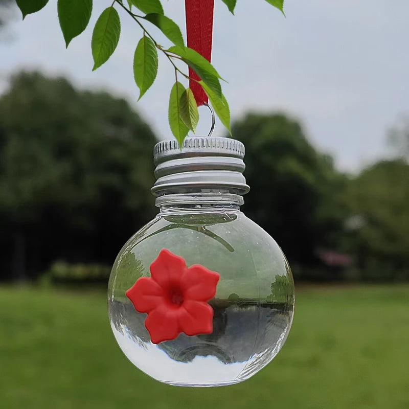 Distributeur d'eau sphérique en verre clair avec une fleur rouge, suspendu à une feuille verte.
