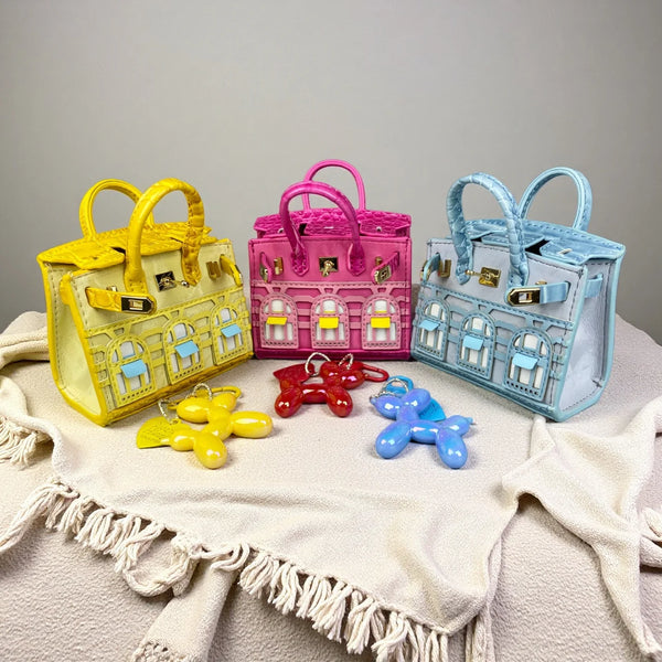 A collection of handcrafted mini house-shaped bags in yellow, pink, and blue, each featuring a puppy keychain charm.