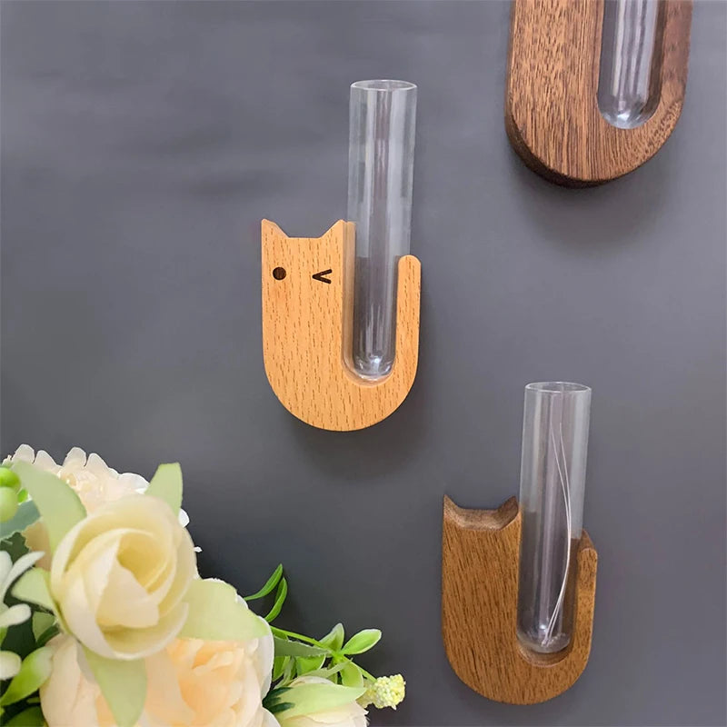A wooden pet whisker collector vase with a glass tube is displayed against a gray background next to white flowers.