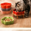 A tabby cat is eating food from a red ceramic slow feeder bowl placed on a wooden stand.