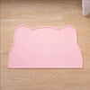 A pink cat head silicone pet feeding mat resting on a light wooden surface.