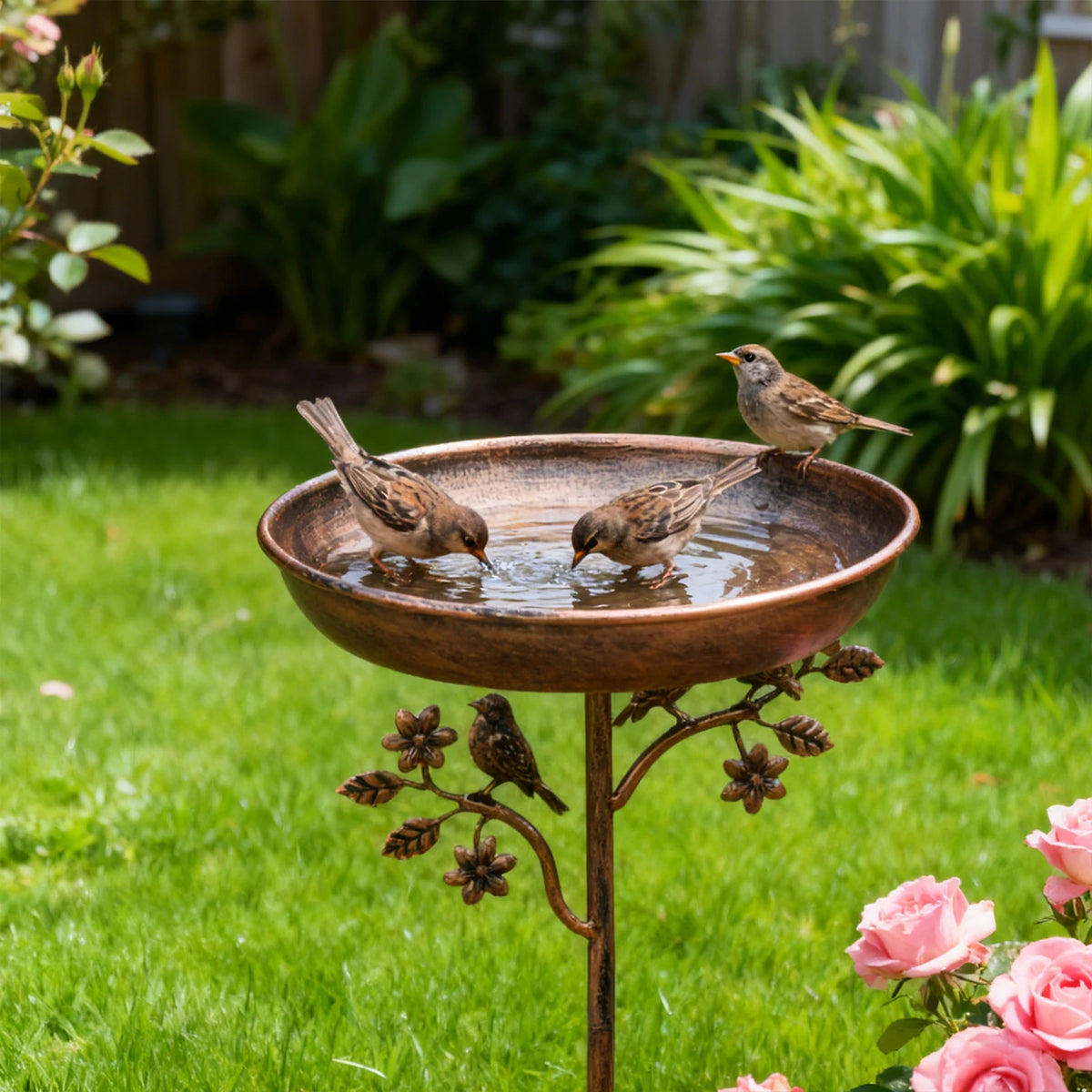 Braune Metallvogelbad mit Wasser, ein Vogel trinkt in einem üppigen grünen Garten.