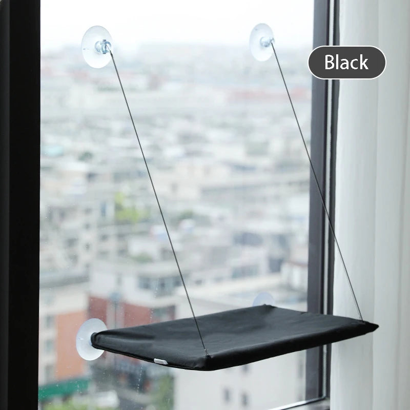 Schwarzes Fenster-Hängemöbel für Katzen, suspendiert in einem Fenster, vor einer städtischen Skyline.