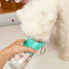 A person holds a teal portable leakproof dog water bottle with a built-in bowl near a white fluffy dog's head.