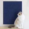 A white and gray cat is sitting on a wooden surface in front of a dark blue textured mat.