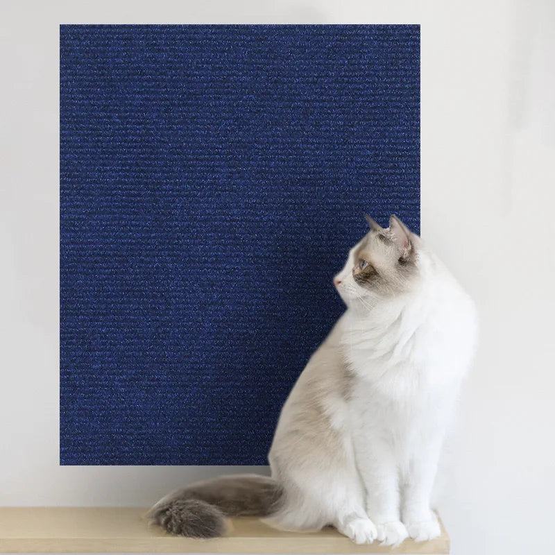 A white and gray cat is sitting on a wooden surface in front of a dark blue textured mat.
