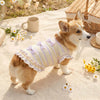A fluffy brown dog wearing a yellow and white striped mesh bow suit lying on a light fabric with small flowers.