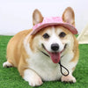 A happy Shiba Inu dog wearing a pink sun hat with ear holes, lying on green grass.