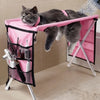 A gray cat is relaxing in a pink foldable pet grooming hammock designed for bathing and nail trimming.