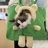 A fluffy cat is visible inside a green pet carrier backpack with bear ears and paws.