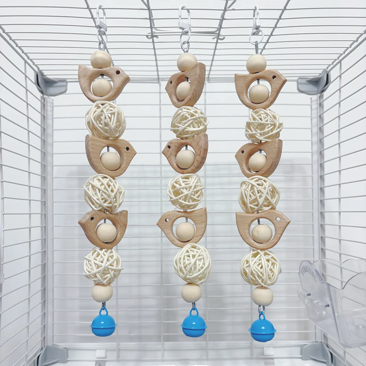 Three decorative wooden parrot swing toys hanging in a clear wire cage