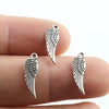 Three antique silver wing charms are shown resting on a person's finger.