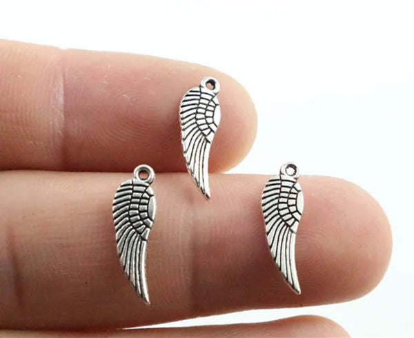 Three antique silver wing charms are shown resting on a person's finger.