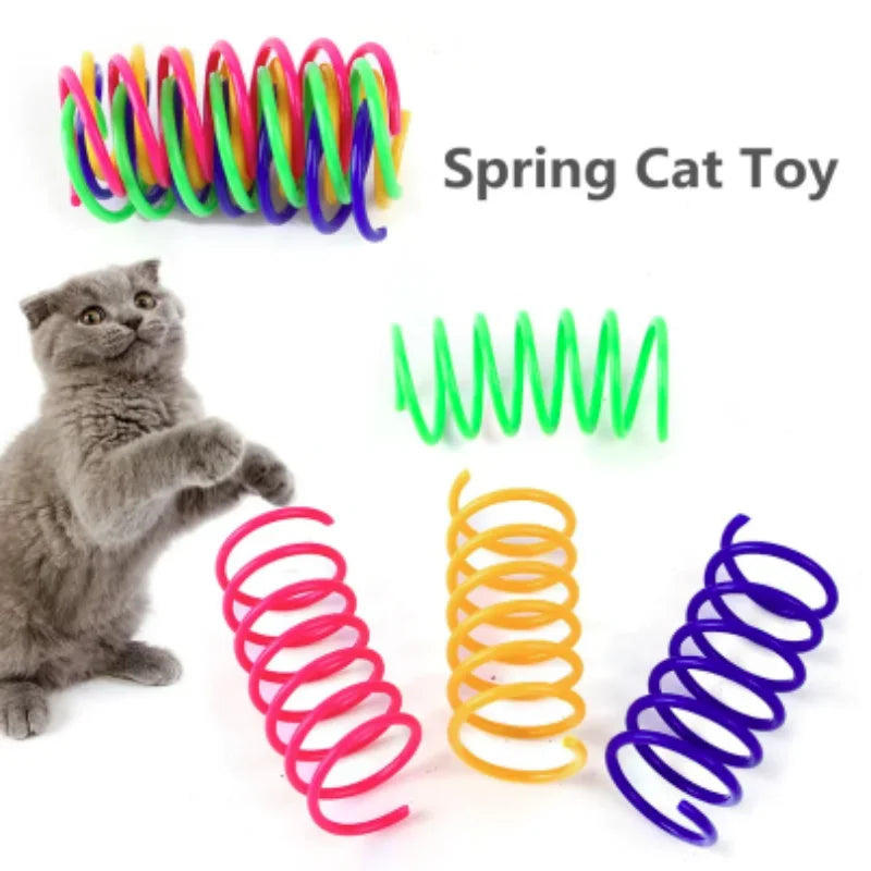 Eine Sammlung farbenfroher Springspielzeuge für Katzen, darunter grüne, lila und orange Spiralen, neben einem grauen Kätzchen