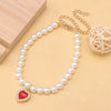 Un délicat collier de perles avec un pendentif de pierre rouge et une chaîne en or, présenté sur un fond clair.