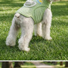 A white dog wearing a light green cooling vest with a built-in fan outdoors on a grassy field.