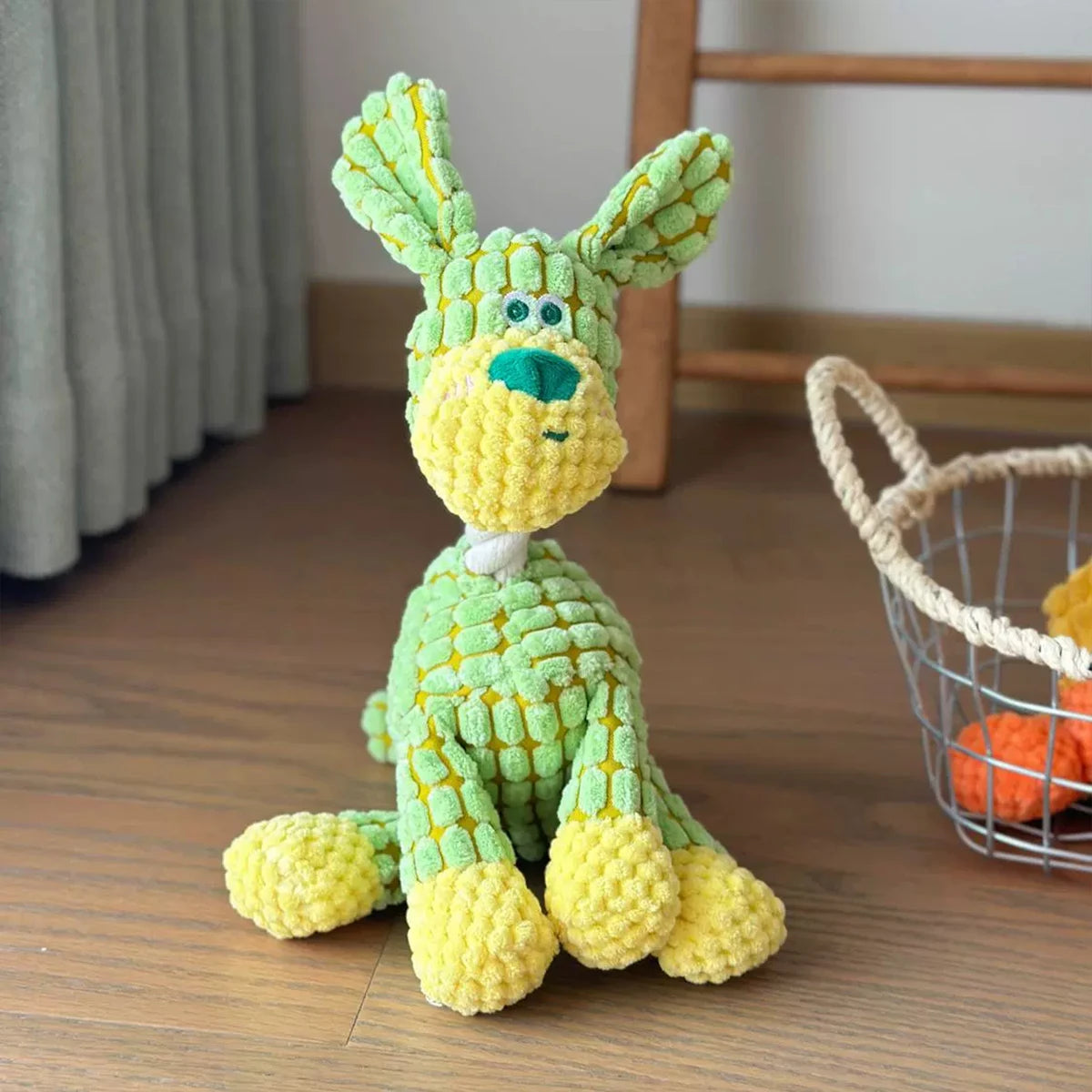 A yellow and green squeaky donkey plush toy with large ears sitting on a wooden floor.
