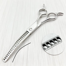 A pair of professional curved pet grooming scissors with silver blades resting on a white wooden surface.