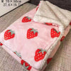 A pink pet blanket with a strawberry pattern and white fluffy trim is displayed on a surface.