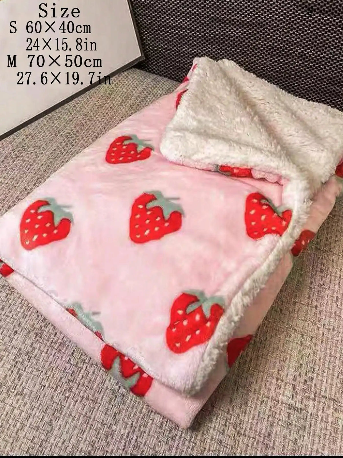 A pink pet blanket with a strawberry pattern and white fluffy trim is displayed on a surface.