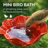 A small bird is drinking water from a red mini bird bath for backyard birds.