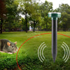 A black ultrasonic pest repeller device with a green top is shown in a grassy outdoor setting with a rodent nearby.