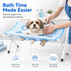 A person is using a blue pet grooming hammock to secure support for grooming and bathing a small dog.