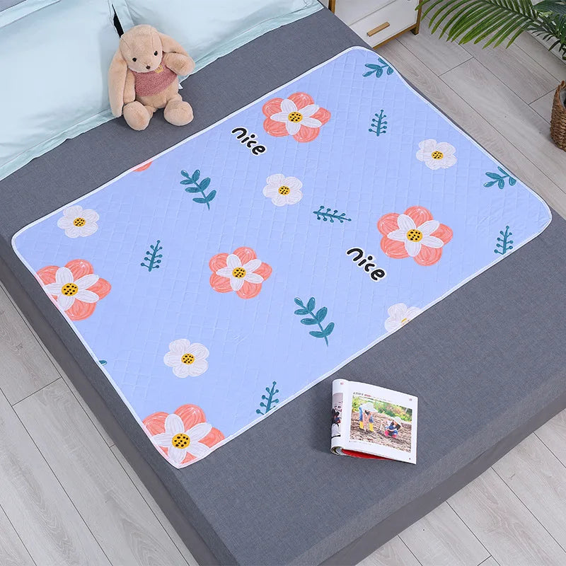 A light blue waterproof cartoon bed protector pad featuring pink and white flowers and green leaves on a gray surface.