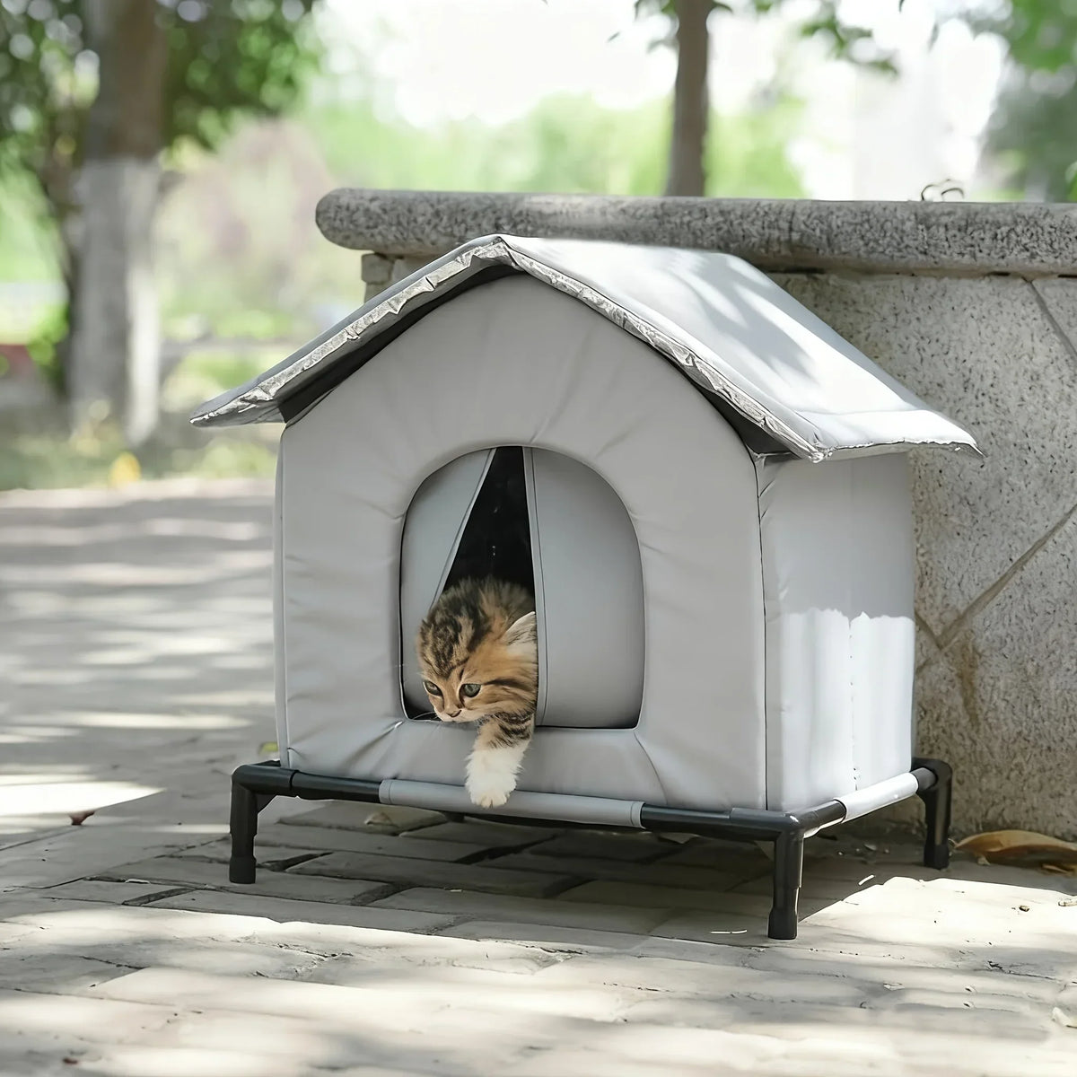 A white, insulated outdoor cat shelter with a pitched roof is placed on a stone ledge.