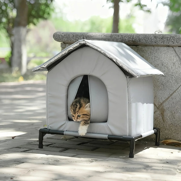 A white, insulated outdoor cat shelter with a pitched roof is placed on a stone ledge.