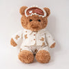 A brown teddy bear plush wearing a light-colored outfit and an eye mask on its head.