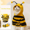 A white cat wearing a yellow and black striped bee-themed hoodie with yellow pom-poms on the ears.