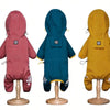 Three waterproof dog raincoats in shades of pink, teal, and yellow displayed on wooden stands.