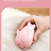 A hand holds a pink electric pet grooming brush with a knot opening on a fluffy white surface.