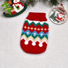 A knitted red dog sweater featuring geometric patterns and white pom-poms, displayed next to Christmas ornaments.