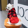 Un perro blanco vistiendo una sudadera con capucha de forro de cuadros rojos y negros con un bolsillo naranja, sentado sobre 