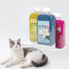 Three bottles of cat litter deodorizing beads in yellow, blue, and pink next to a cat.