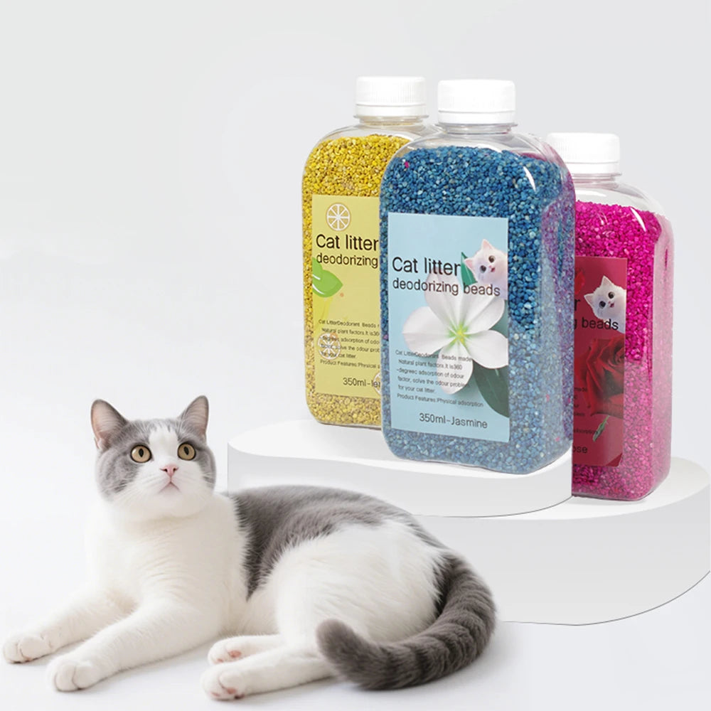 Three bottles of cat litter deodorizing beads in yellow, blue, and pink next to a cat.