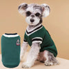 A small, fluffy dog wearing a dark green V-neck knit vest with white trim.