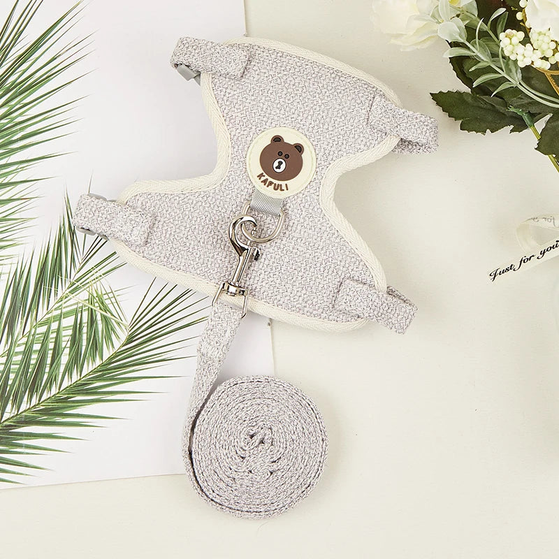 A light gray padded rabbit harness and leash set with a round tag and coiled leash shown on a white surface.
